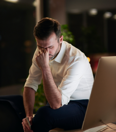 Homem cansado diante do computador, à noite, com a mão no rosto