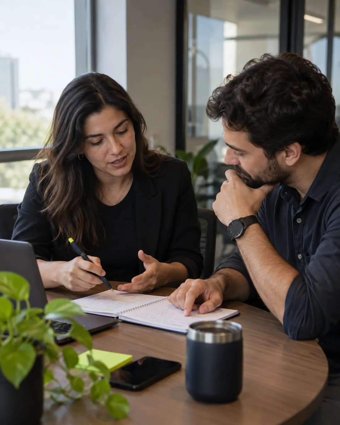 Duas pessoas conversam à mesa sobre anotações em um caderno, em clima de parceria